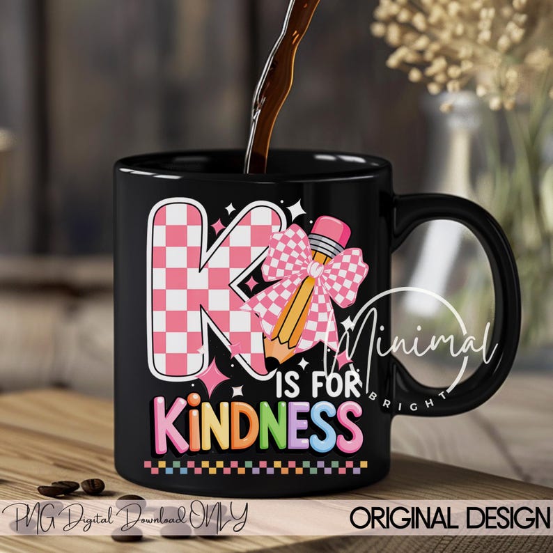 May include: Black coffee mug with the words "K is for Kindness" in colorful letters. The letter "K" is in a pink and white checkered pattern, and a pencil with a pink bow is next to it. The mug has a black handle.
