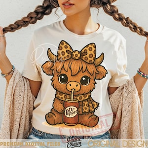 May include: A cream-colored t-shirt featuring a cartoon Highland cow with a bow, scarf, and a Dr. Pepper can. The cow is brown with large eyes and a spotted bow and scarf. The Dr. Pepper can is brown and red.