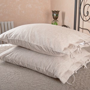 May include: Two beige linen pillowcases with ties. The pillowcases are stacked on top of each other and have a subtle texture.
