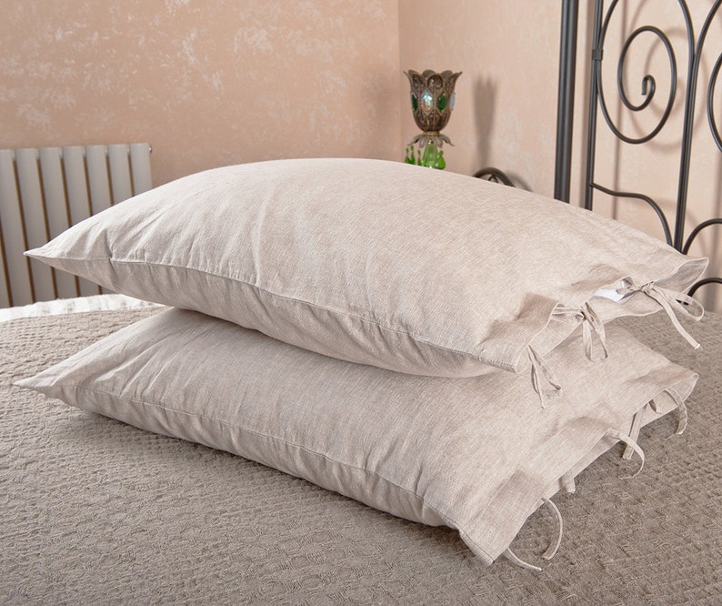 May include: Two beige linen pillowcases with ties. The pillowcases are stacked on top of each other and have a subtle texture.