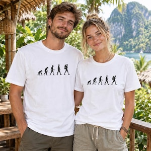 Könnte beinhalten: Ein weißes kurzärmeliges T-Shirt mit einem schwarzen Grafikdruck der menschlichen Evolutionssequenz, beginnend mit einem Primaten und fortschreitend bis zu einer modernen menschlichen Figur mit Rucksack, zentriert auf dem Brustbereich.