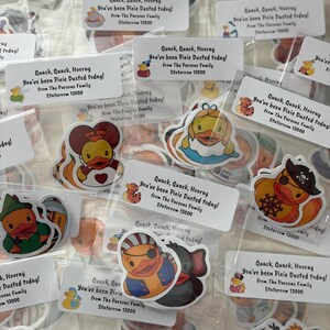 May include: A collection of rubber duck stickers in individual clear plastic bags, each with a white label reading: Quack, Quack, Hooray, You've been Pixie Dusted today! from The Parsons Family Stateroom 13000. The stickers feature various duck characters.