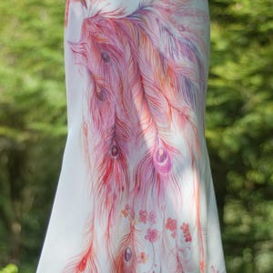 May include: A floor-length white skirt featuring a detailed hand-painted design of a large bird with long, flowing tail feathers in shades of pink, orange, and purple, accented with small floral motifs scattered across the fabric.