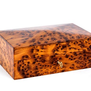 May include: A wooden box with a burl wood finish and a brass latch. The box has a rectangular shape and is made of a dark brown wood with a natural grain pattern.
