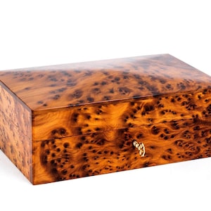 May include: A rectangular wooden box with a polished finish and a distinct burl wood grain pattern in shades of amber and dark brown. The box features a hinged lid and a small, gold-colored metal key inserted into the front lock mechanism.