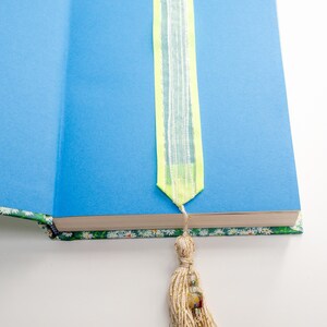 May include: A book with a blue cover and a bookmark with a yellow and white striped ribbon and a tassel with beads and a gold fish charm.