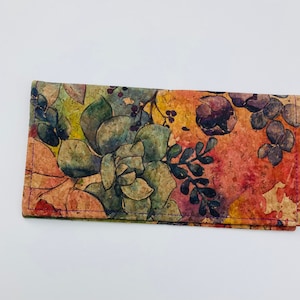 May include: A brown and orange wallet with a floral pattern featuring succulents and leaves. The wallet is made of cork and has a purple stitching around the edges.