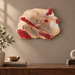 May include: A wall clock with an irregular, geode-inspired shape featuring a cream and beige marbled surface. It is accented with textured, deep red crystalline clusters and small, iridescent marquise-shaped markers. Gold-tone clock hands.