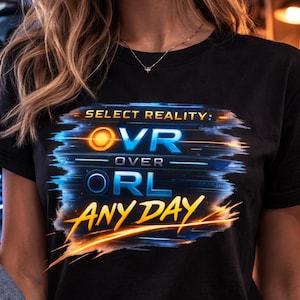 May include: Black t-shirt with the text "SELECT REALITY: VR OVER IRL ANY DAY" in blue and orange. The shirt is worn with blue jeans and a denim jacket. A computer setup is visible in the background.