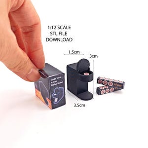 May include: A black 1:12 scale model of a single-serve coffee maker with a K-Cup pod. The model is 3.5 cm wide, 3 cm deep, and 1.5 cm tall. The model is accompanied by two packs of K-Cup pods.