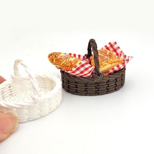 May include: Miniature picnic basket with a loaf of bread and a red and white checkered napkin. A white woven basket is next to the picnic basket. The baskets are likely for a dollhouse or other miniature scene.