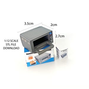 Puede incluir: Un horno tostador eléctrico en miniatura gris a escala 1:12 con una puerta negra y un panel de control azul. El horno mide 3,5 cm de ancho, 2 cm de profundidad y 2,7 cm de alto. El horno está sobre una superficie blanca con una caja azul y blanca a su lado.