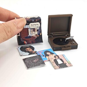 May include: Miniature brown record player with a black record and silver tone arm. Includes miniature album covers with various album art. One album cover has the text "Build My Home".