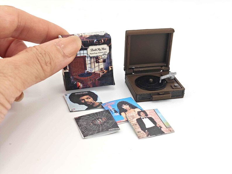 May include: Miniature brown record player with a black record and silver tone arm. Includes miniature album covers with various album art. One album cover has the text "Build My Home".