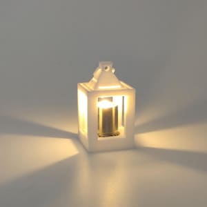 Può includere: Una piccola luce decorativa bianca a forma di lanterna con un interno caldo e luminoso. La lanterna ha una forma rettangolare con un manico in alto. La luce proietta un bagliore morbido e diffuso, creando un'atmosfera accogliente.