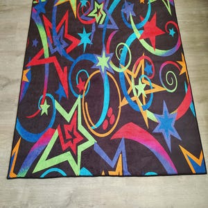 May include: A black rug with a colourful design featuring stars, swirls, and abstract shapes in shades of red, orange, yellow, green, blue, and purple.
