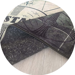 Pu&ograve; includere: Un tappeto rotondo con un design a mappa vintage. Il tappeto presenta uno sfondo bianco sporco invecchiato con grafiche a bussola nere e grigie e la parola "STAR". Il lato inferiore del tappeto &egrave; un materiale grigio scuro strutturato.