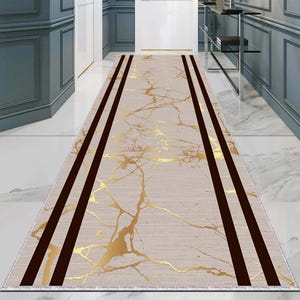 Puede incluir: Una alfombra de pasillo beige con un patrón de mármol dorado y tres rayas negras que recorren la longitud de la alfombra.