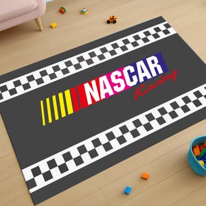 May include: A grey and black chequered rug with the words "NASCAR Racing" in colourful letters. The rug is designed to look like a race track.