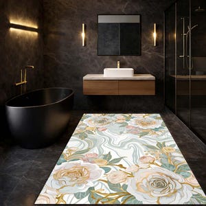 May include: A rectangular bathroom rug with a floral design. The rug features large white, gold, and pink roses with green leaves and a light blue background. It is placed on a dark grey tiled floor.