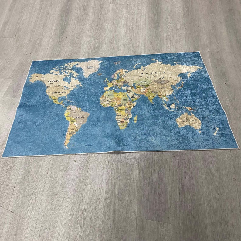 May include: A rectangular world map rug with a blue background and a detailed depiction of the continents in shades of beige, brown, and yellow. The rug has a white border and is placed on a wooden floor.