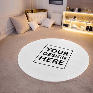 Pu&ograve; includere: Un tappeto rotondo bianco con la scritta "YOUR DESIGN HERE" in nero, in grassetto. Il tappeto &egrave; posizionato su un tappeto di colore chiaro, con cuscini e mobili sullo sfondo.