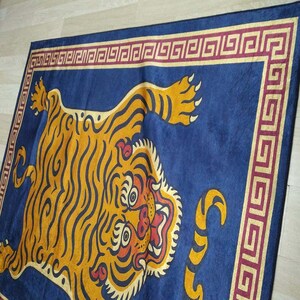 May include: A rectangular blue rug featuring a detailed illustration of a tiger. The tiger is depicted in shades of yellow and orange with black stripes. The rug has a decorative border with a geometric pattern in burgundy and gold.