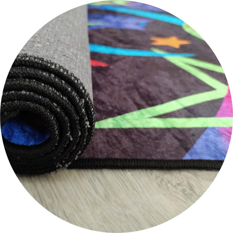 Pu&ograve; includere: Tappeto arrotolato con bordo nero e motivo geometrico colorato. Il motivo include forme blu, verdi, arancioni e viola su sfondo scuro. Il lato inferiore del tappeto &egrave; grigio e il bordo arrotolato rivela un interno blu.