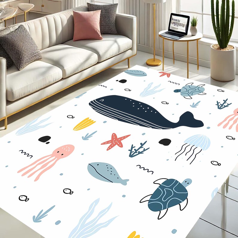 K&ouml;nnte beinhalten: Wei&szlig;er Teppich mit einem farbenfrohen Design zum Thema Meer. Der Teppich zeigt einen Wal, einen Tintenfisch, einen Seestern, eine Qualle, einen Fisch und Schildkr&ouml;ten.