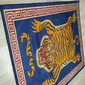 May include: A rectangular blue rug featuring a stylized orange tiger with black stripes. The tiger is centered on the rug, with a red and gold border. The rug has a decorative geometric pattern.