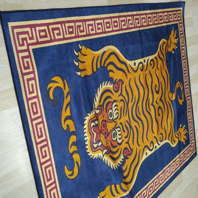 May include: A rectangular blue rug featuring a stylized orange tiger with black stripes. The tiger is centered on the rug, with a red and gold border. The rug has a decorative geometric pattern.
