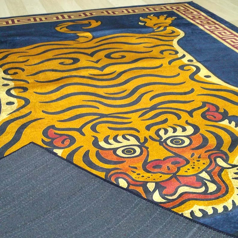 May include: A rectangular rug featuring a stylized tiger design. The tiger is primarily yellow and orange with black outlines, set against a dark blue background. The rug has a decorative border.