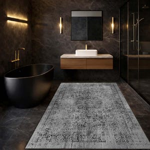 May include: A grey and black patterned rug in a modern bathroom. The rug is rectangular with a distressed, vintage-inspired design. The bathroom features a black bathtub, a wooden vanity, and a glass shower enclosure.