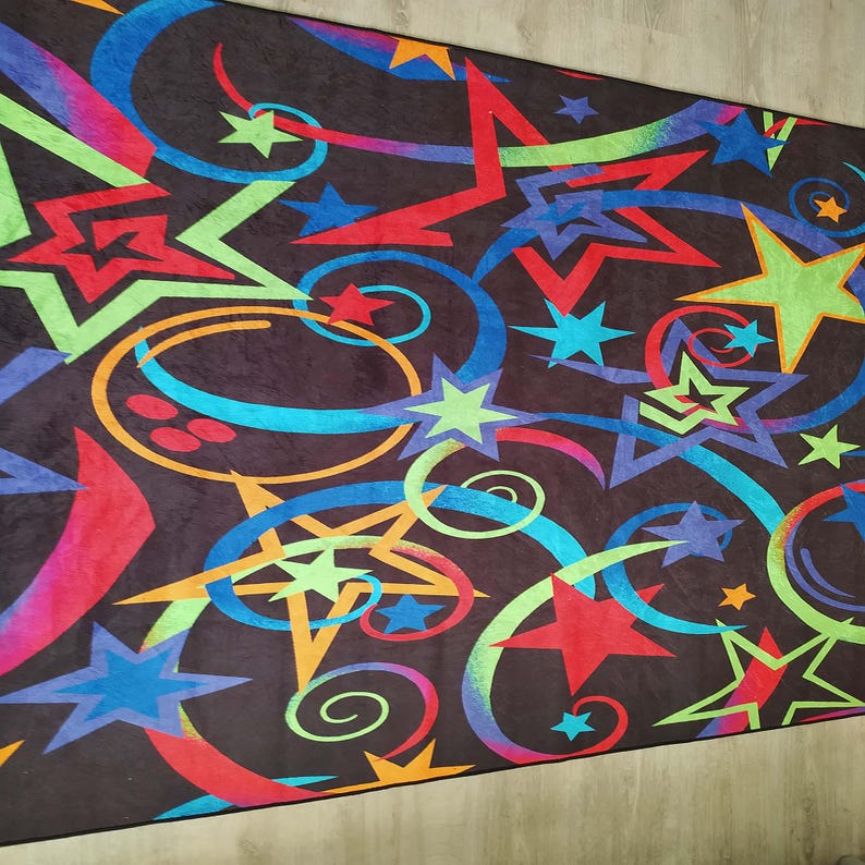 May include: A black rug with a colourful design of stars and swirls. The stars are in various colours, including red, green, blue, and yellow. The swirls are in shades of blue, green, and orange.