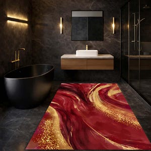Op de afbeelding: Een rechthoekige badmat met een abstract rood en goud ontwerp. De mat heeft wervelende patronen van diep rood en goud, wat een luxe en artistieke uitstraling creëert. De mat ligt op een donkergrijze tegelvloer in een moderne badkamer.