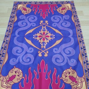 Puede incluir: Una alfombra m&aacute;gica azul y morada con un dise&ntilde;o dorado y rojo. La alfombra tiene un patr&oacute;n repetitivo de llamas y remolinos. Hay cuatro cabezas de le&oacute;n en las esquinas de la alfombra.