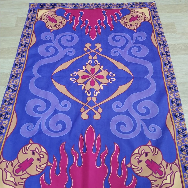 Puede incluir: Una alfombra m&aacute;gica azul y morada con un dise&ntilde;o dorado y rojo. La alfombra tiene un patr&oacute;n repetitivo de llamas y remolinos. Hay cuatro cabezas de le&oacute;n en las esquinas de la alfombra.