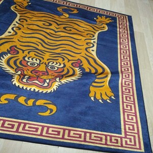 May include: A rectangular blue rug featuring a stylized tiger design in shades of yellow, orange, and black. The tiger's face is prominently displayed, with a detailed border in gold and burgundy.