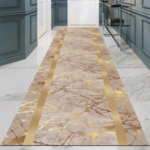 Può includere: Un tappeto da corridoio beige e oro con un motivo a marmi e un bordo geometrico. Il tappeto ha una lucentezza discreta e una sensazione di lusso.