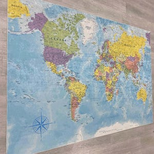 May include: A large world map with a blue ocean background and colorful continents. The map includes country names and a compass rose in the lower left corner. The map is mounted on a white frame.