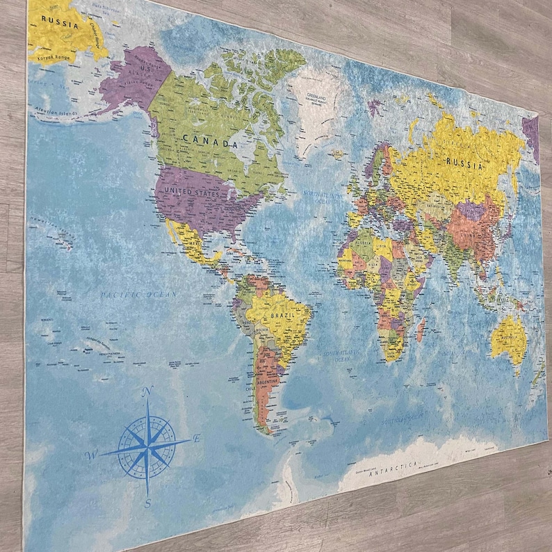 May include: A large world map with a blue ocean background and colorful continents. The map includes country names and a compass rose in the lower left corner. The map is mounted on a white frame.