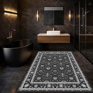 Può includere: Un tappeto da bagno rettangolare grigio scuro con un motivo floreale dettagliato e un bordo bianco. Il tappeto è posizionato su un pavimento piastrellato grigio scuro in un bagno moderno, con una vasca da bagno nera e un mobile lavabo in legno.