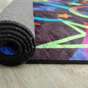 May include: A rolled up black and grey rug with a colourful geometric pattern featuring green, blue, pink, and yellow. The rug has a black border.