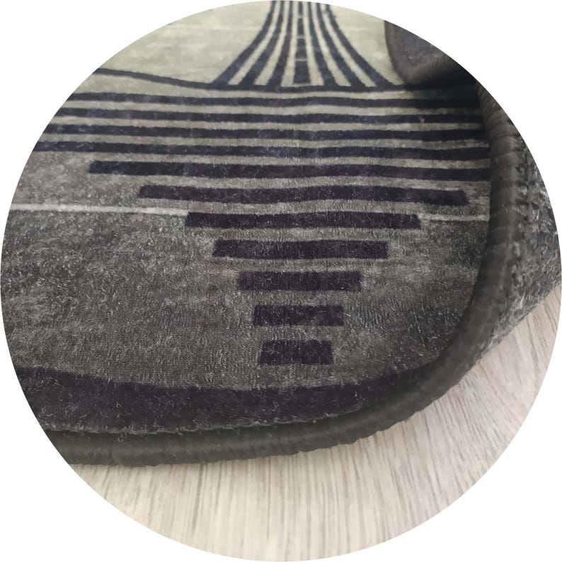 Pu&ograve; includere: Primo piano di un tappeto grigio con un design geometrico. Il tappeto presenta linee orizzontali e verticali blu scuro, creando un motivo moderno. I bordi sono rifiniti con un bordo scuro e il tappeto ha un aspetto morbido e strutturato.