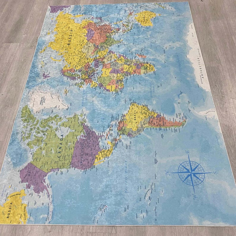 May include: A large, rectangular rug featuring a world map design. The map displays continents in various colors, with country borders and names. A compass rose is in the lower right corner. The rug has a light blue background.