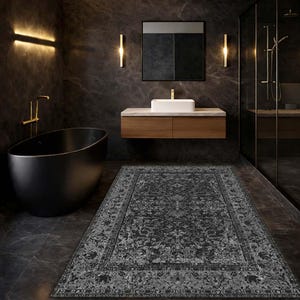 May include: A dark grey rectangular rug with an intricate floral design lies in a modern bathroom. The rug has a detailed border and a central medallion. The bathroom features a black bathtub, a wooden vanity, and dark grey walls.