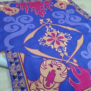 Puede incluir: Una alfombra m&aacute;gica azul y morada con un dise&ntilde;o dorado y rosa. La alfombra tiene una cabeza de tigre en la parte inferior y un dise&ntilde;o floral en el centro.