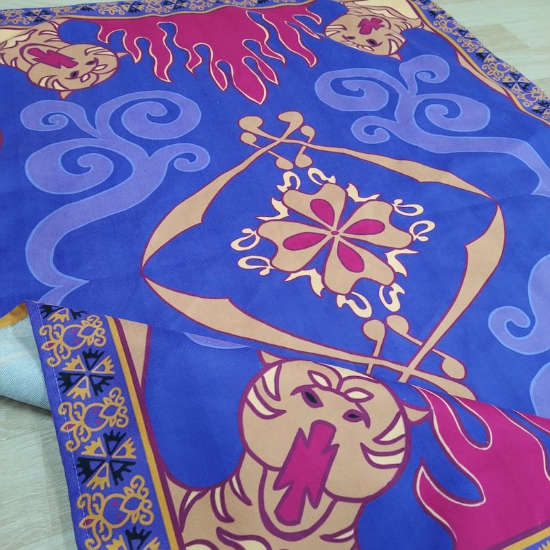 Puede incluir: Una alfombra m&aacute;gica azul y morada con un dise&ntilde;o dorado y rosa. La alfombra tiene una cabeza de tigre en la parte inferior y un dise&ntilde;o floral en el centro.