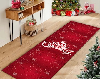 Op de afbeelding: Een rode kerst loper met witte sneeuwvlokken en de tekst "Merry Christmas". De rechthoekige loper ligt op een houten vloer. Een kerstboom en feestelijke decoraties zijn zichtbaar op de achtergrond.