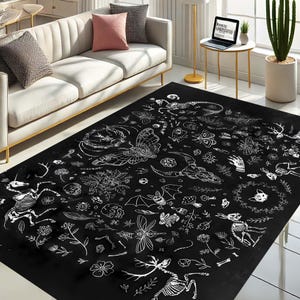 Pode incluir: Tapete preto e branco com um design caprichoso que apresenta uma variedade de ilustra&ccedil;&otilde;es, incluindo esqueletos, borboletas, cr&acirc;nios e outros elementos inspirados na natureza.